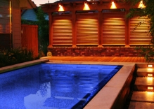 Night-Shot-modern-swimming-pool-spill-over-edge-arbor-and-louvered-wall.-concrete-stepping-stones-and-mexican-beach-pebbles